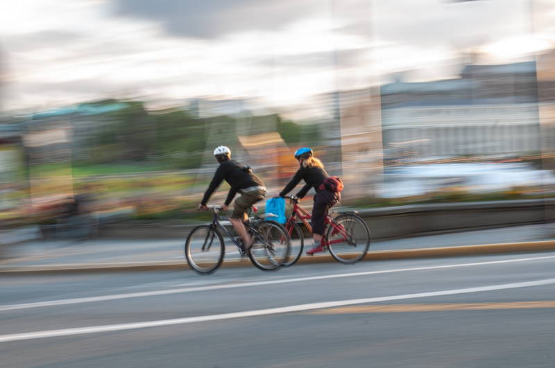 Couple of cyclists in urban setting riding bicycles through streets with speed blur. Stock Photography Free for Commercial Use.