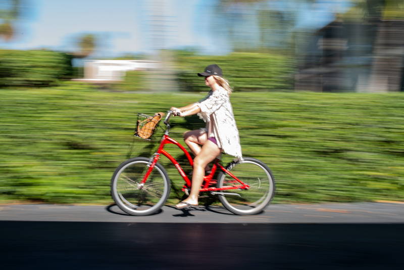Woman Biking on sidewalk in front of green bushes with speed blur. Stock Photography Free for Commercial Use.