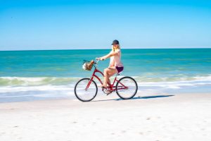 Woman Biking on tropical sand in front of waves. Stock Photography Free for Commercial Use.