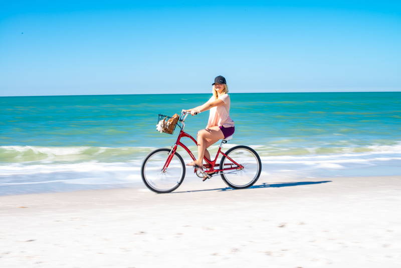 Woman Biking on tropical sand in front of waves. Stock Photography Free for Commercial Use.