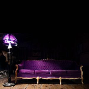 Purple couch under purple lamp with wooden hardwood floor, vintage retro velvet fabric couch. Stock Photography Free for Commercial Use.