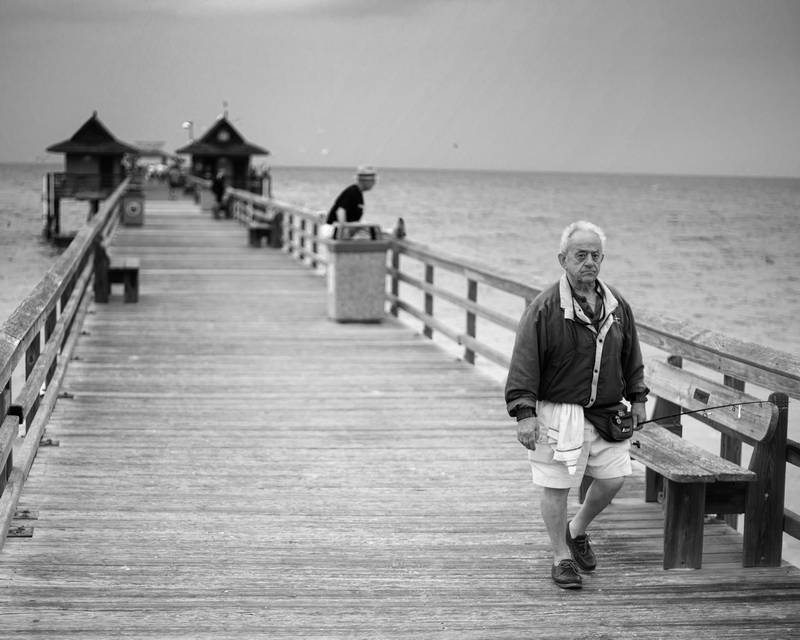 Long pier in black in white, old man walking, beautiful ocean. Stock Photography Free for Commercial Use.