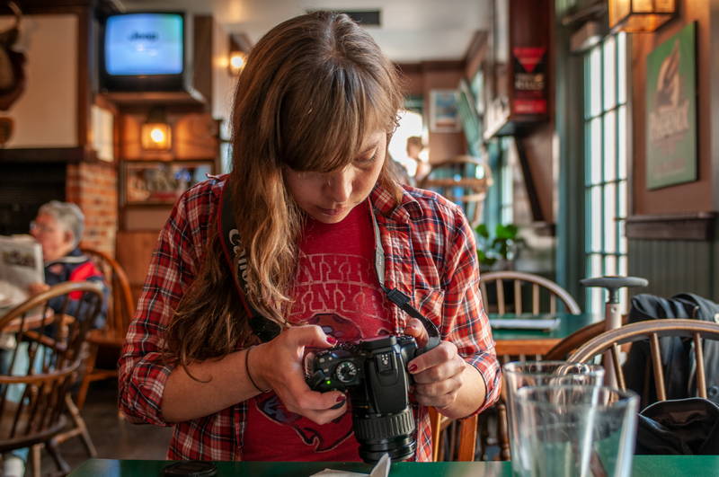 Woman in pub using digital camera, adjusting settings on DSLR. Stock Photography Free for Commercial Use.