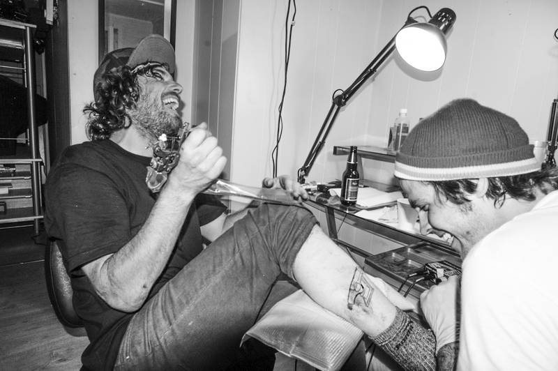 Tattoo artist in small studio, black and white with punk rock men laughing. Stock Photography Free for Commercial Use.